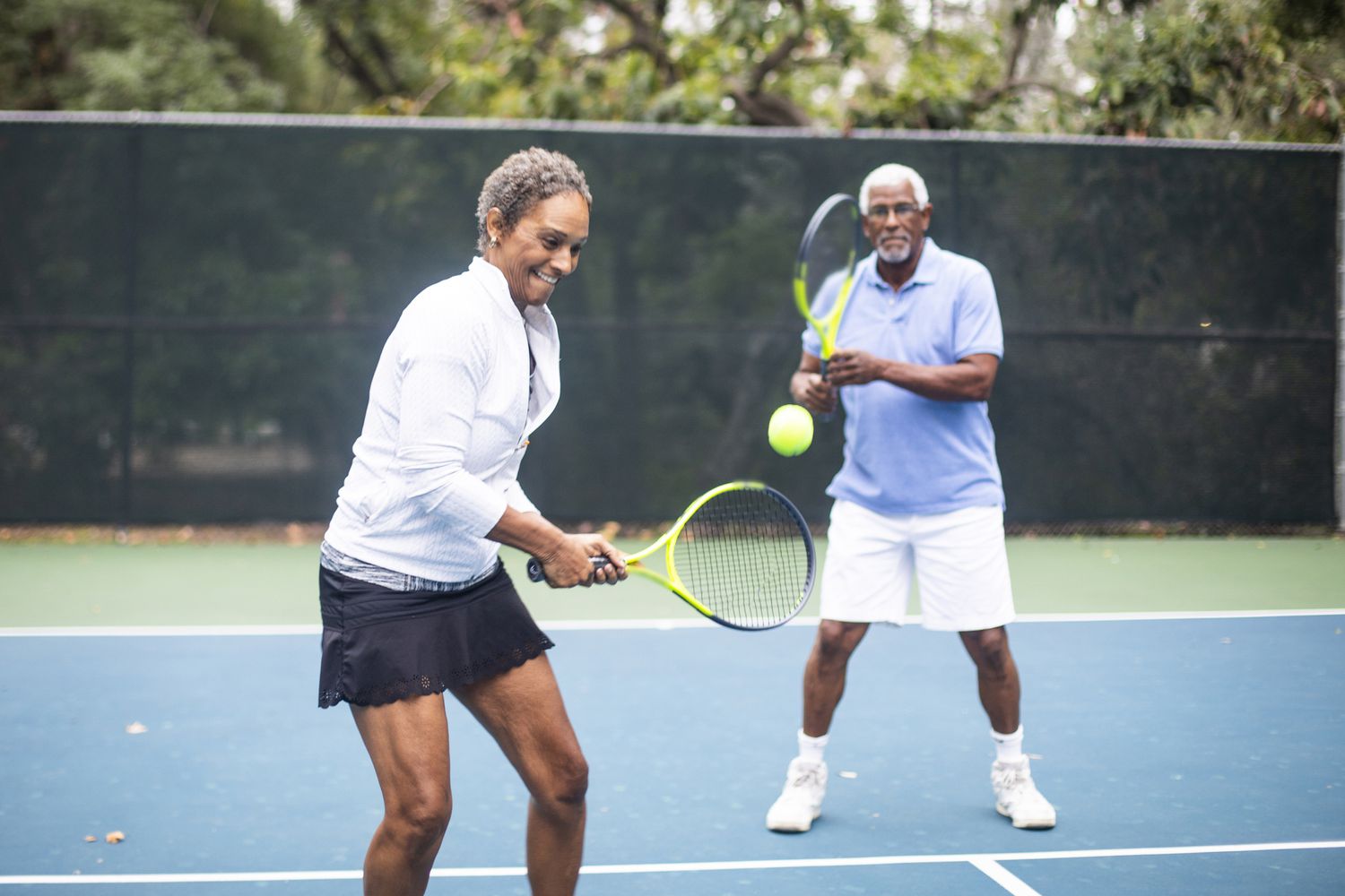A Senior Black Couple Playing Doubles Tennis on a cloudy morning