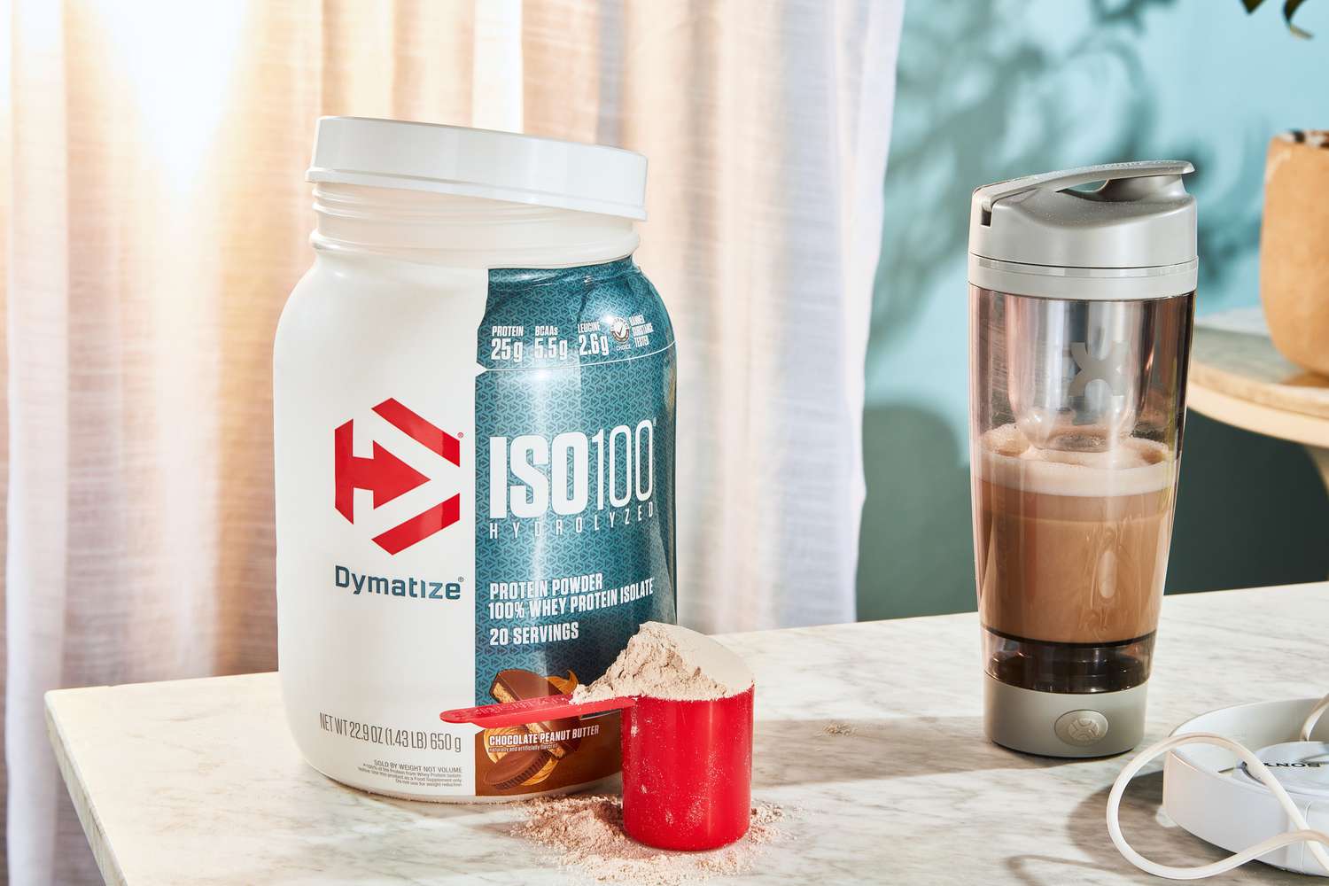 Dymatize ISO100 Whey Protein Powder in a scoop next to its container and a bottle blender