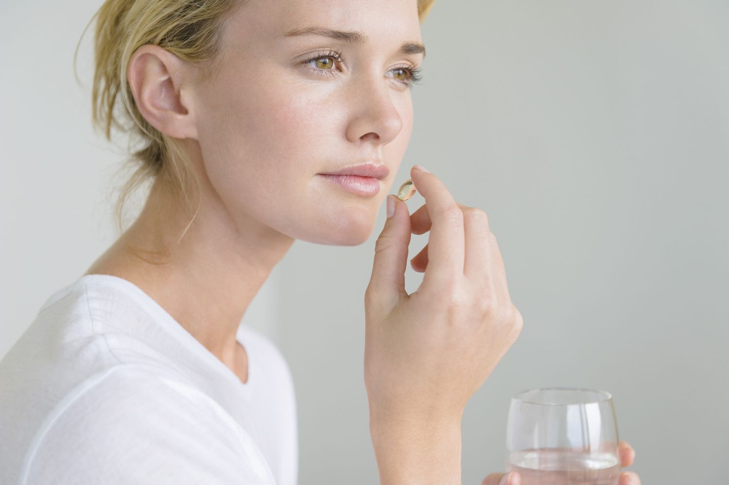 Woman taking an oral supplement with a glass of water