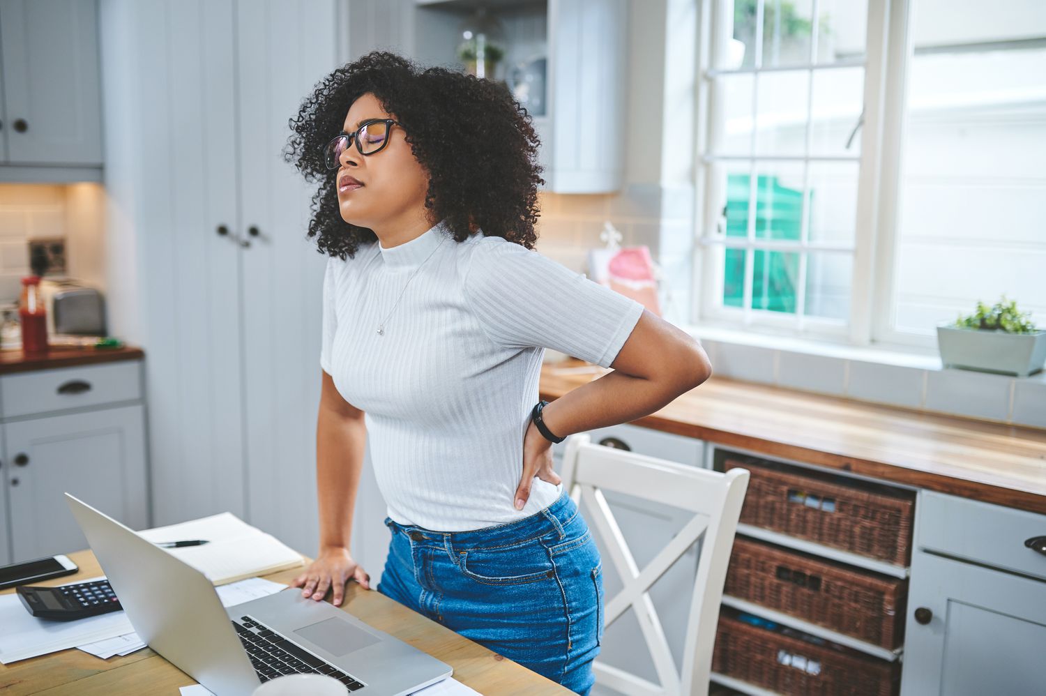 Young Black woman with back pain standing at desk