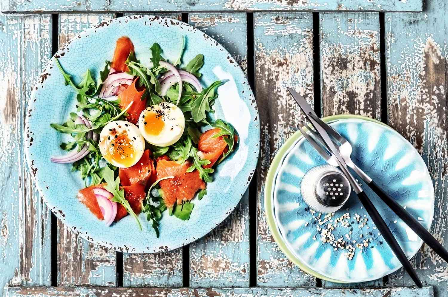 Arugula salad with smoked salmon, red onion and boiled eggs on wooden, blue background
