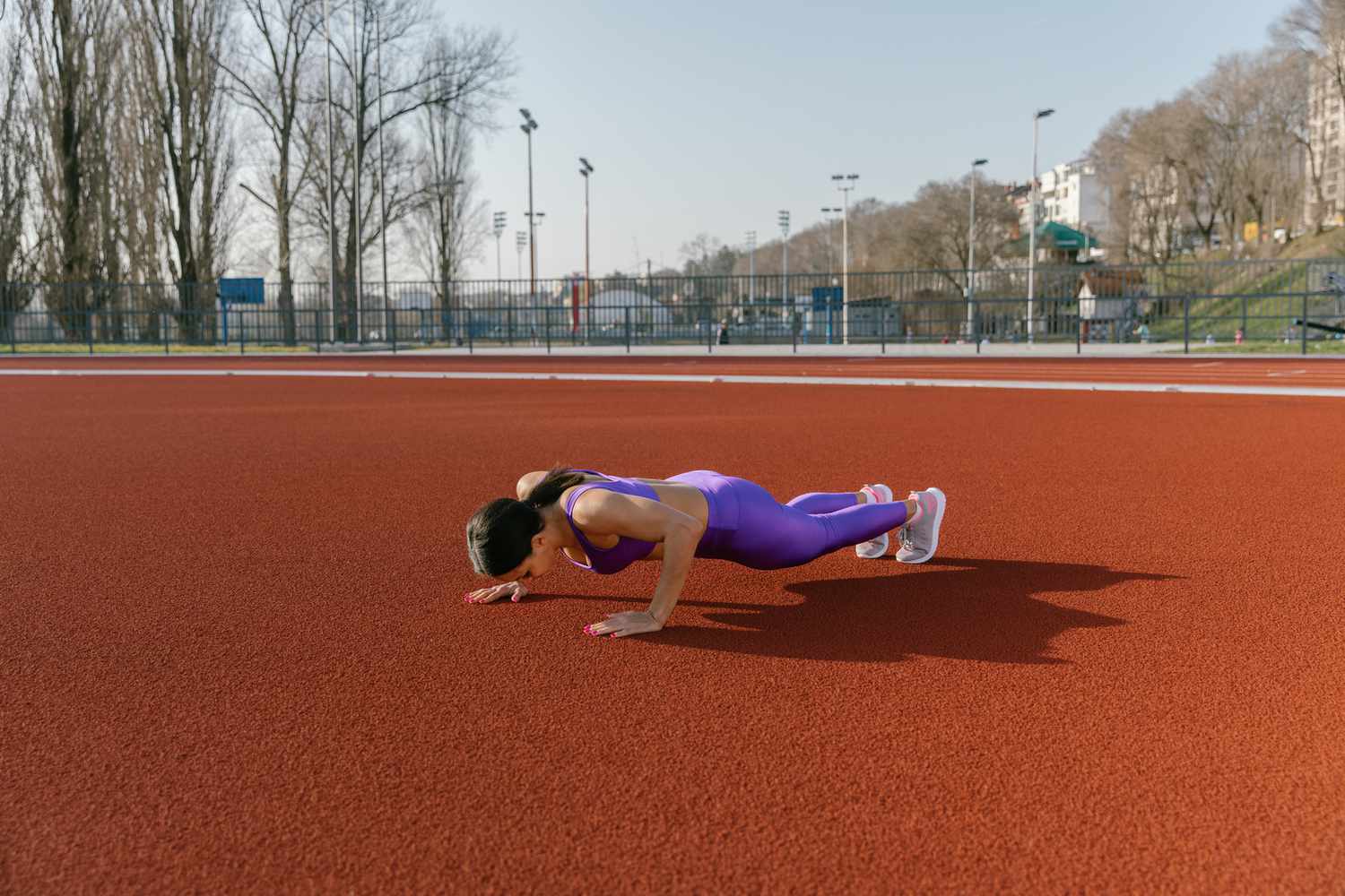 Woman doing a workout outdoors, she is doing push ups at the athletic stadium.