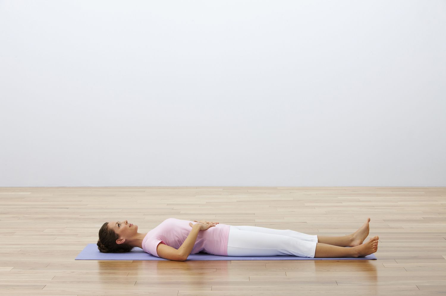 Woman lying on back on yoga mat with hands on abdomen