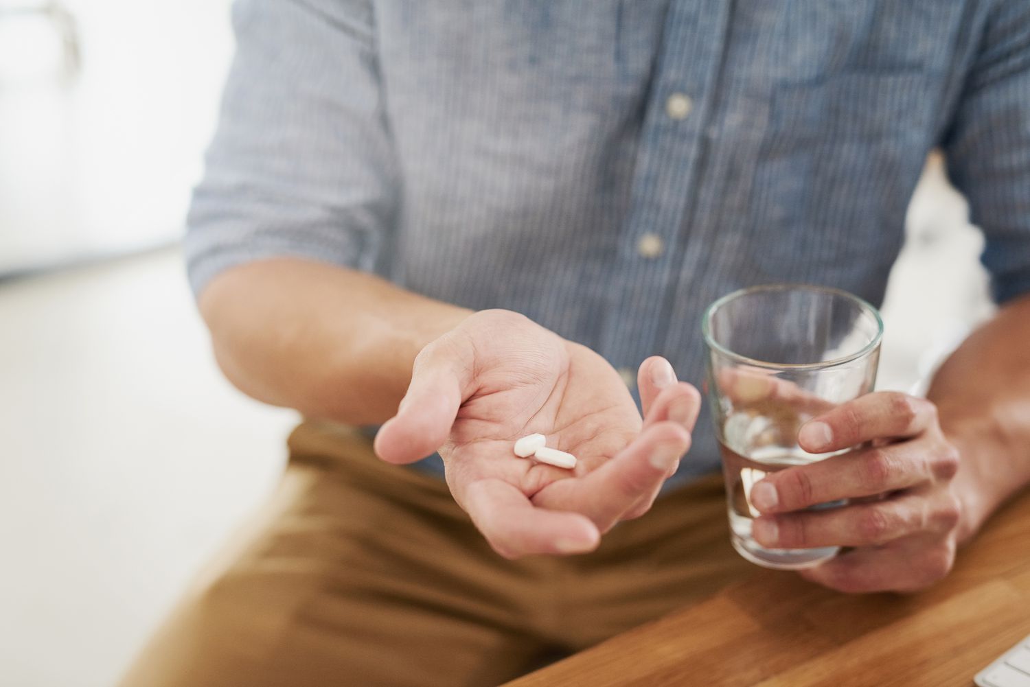 Man taking white supplement pills with water