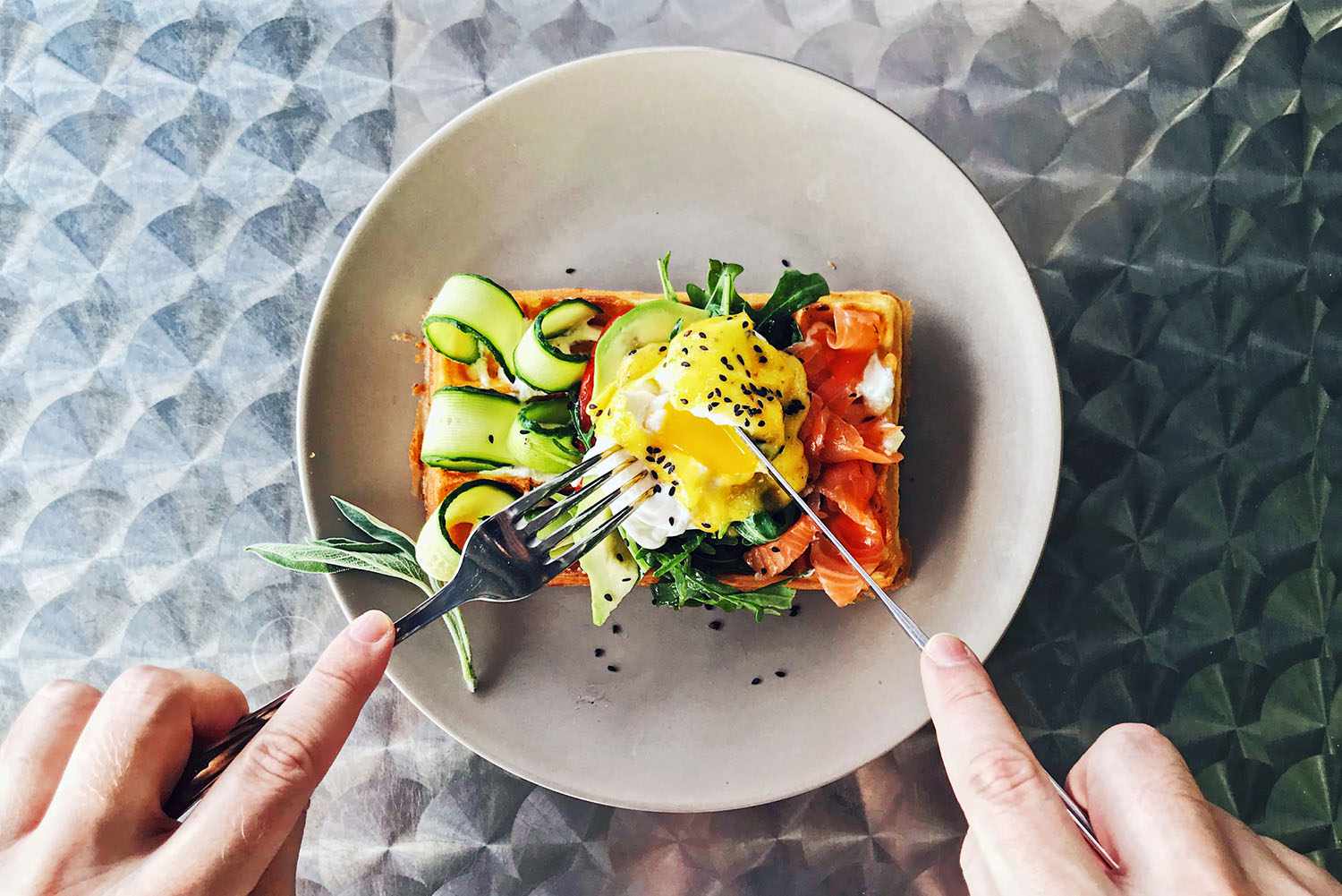 Eating brunch with waffle, avocado, cucumber, salmon and poached egg, personal perspective