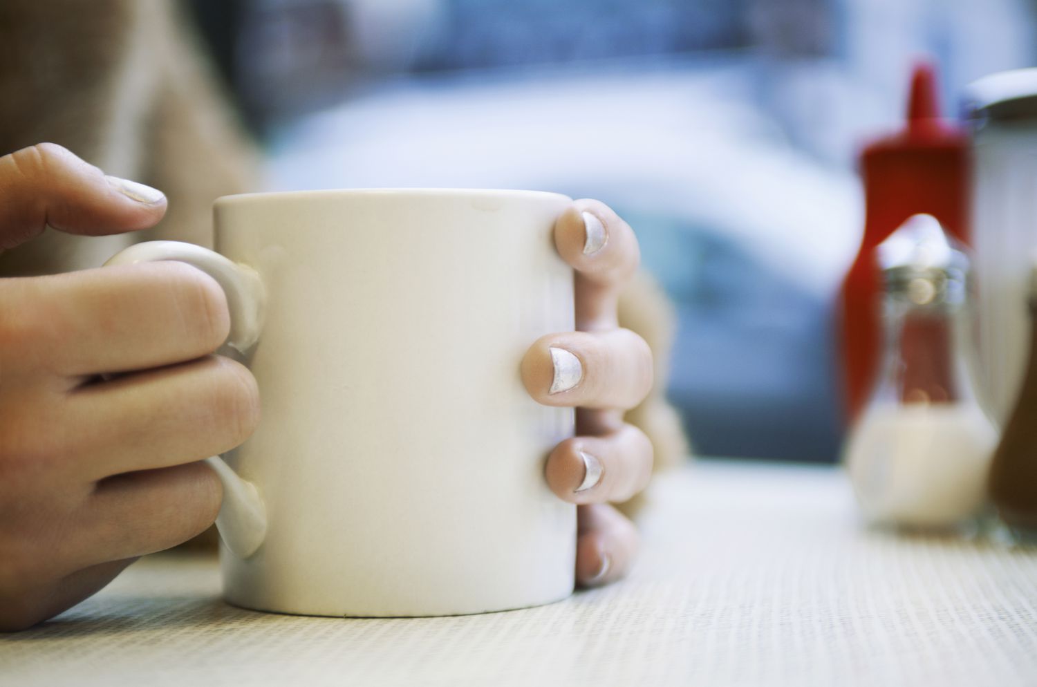 close up of hands holding cup of coffee in cafe