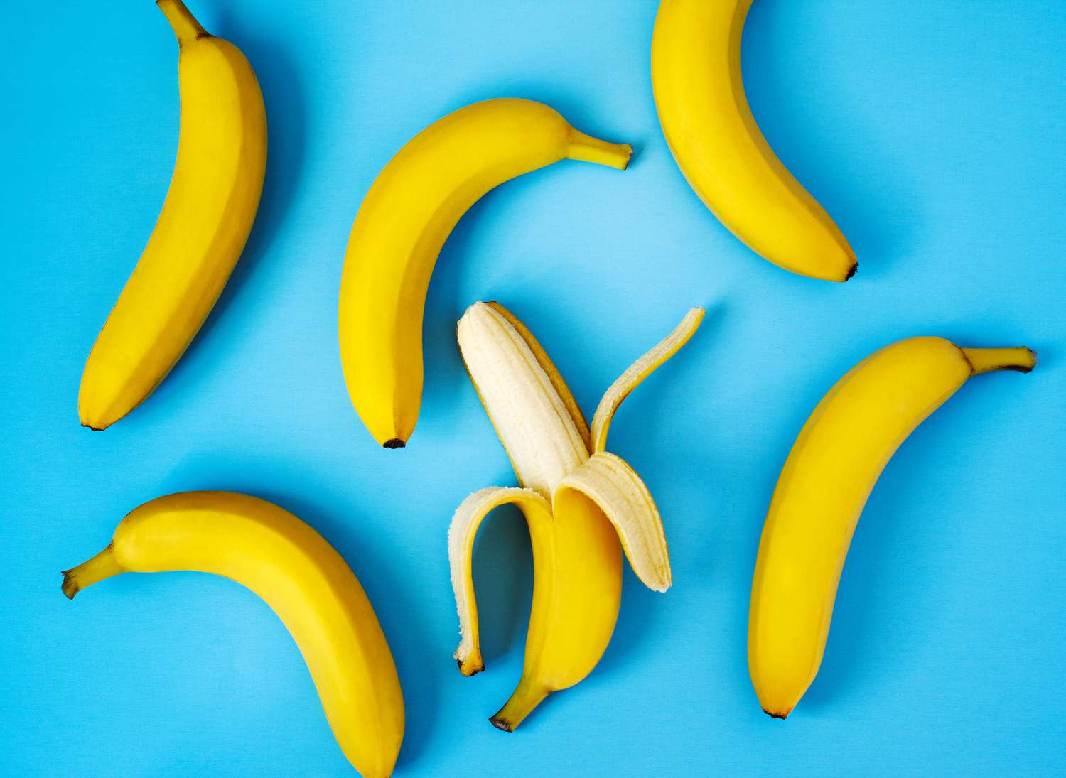 Six bananas, one peeled, on a bright blue background