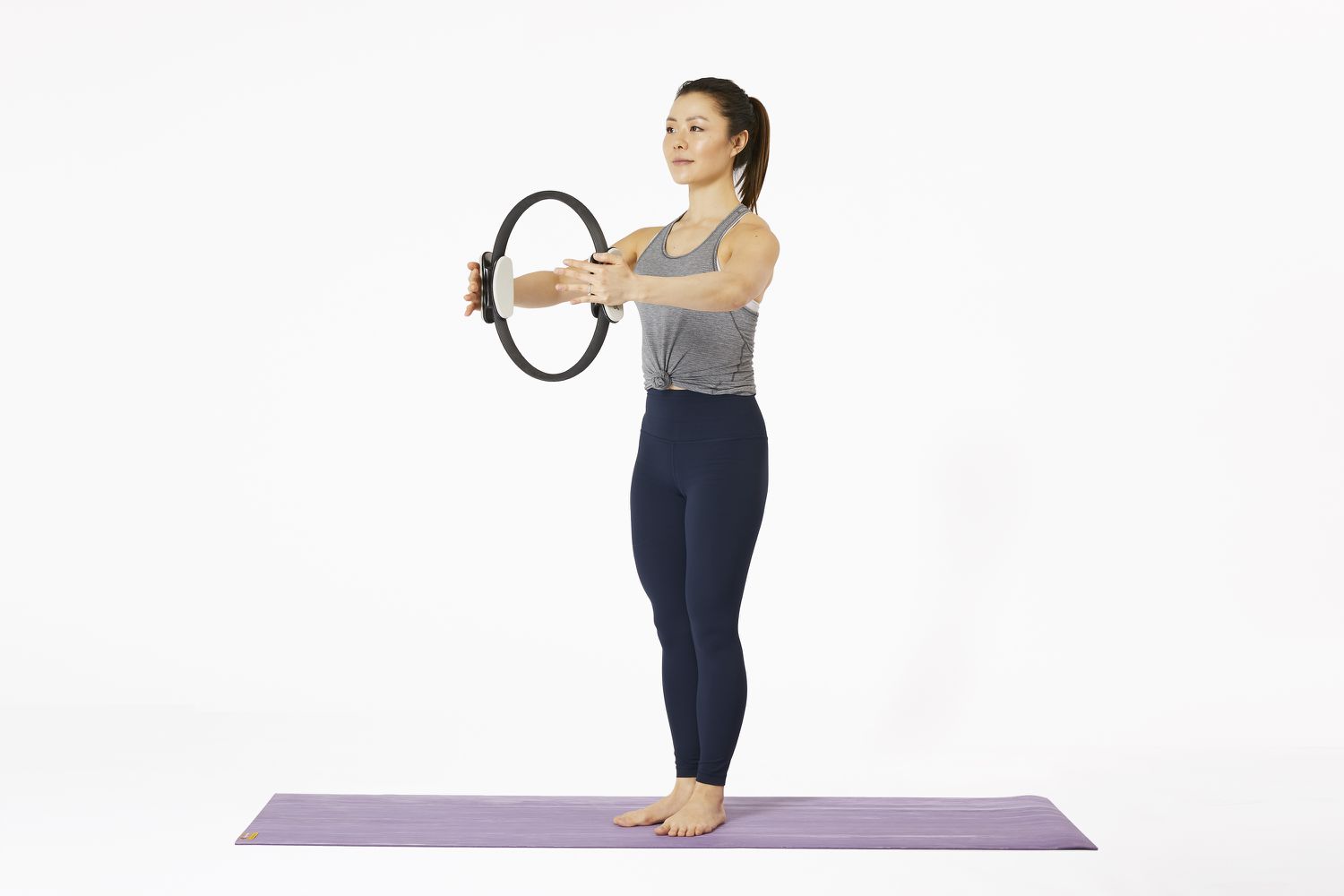 Woman standing on yoga mat using Pilates Magic Circle