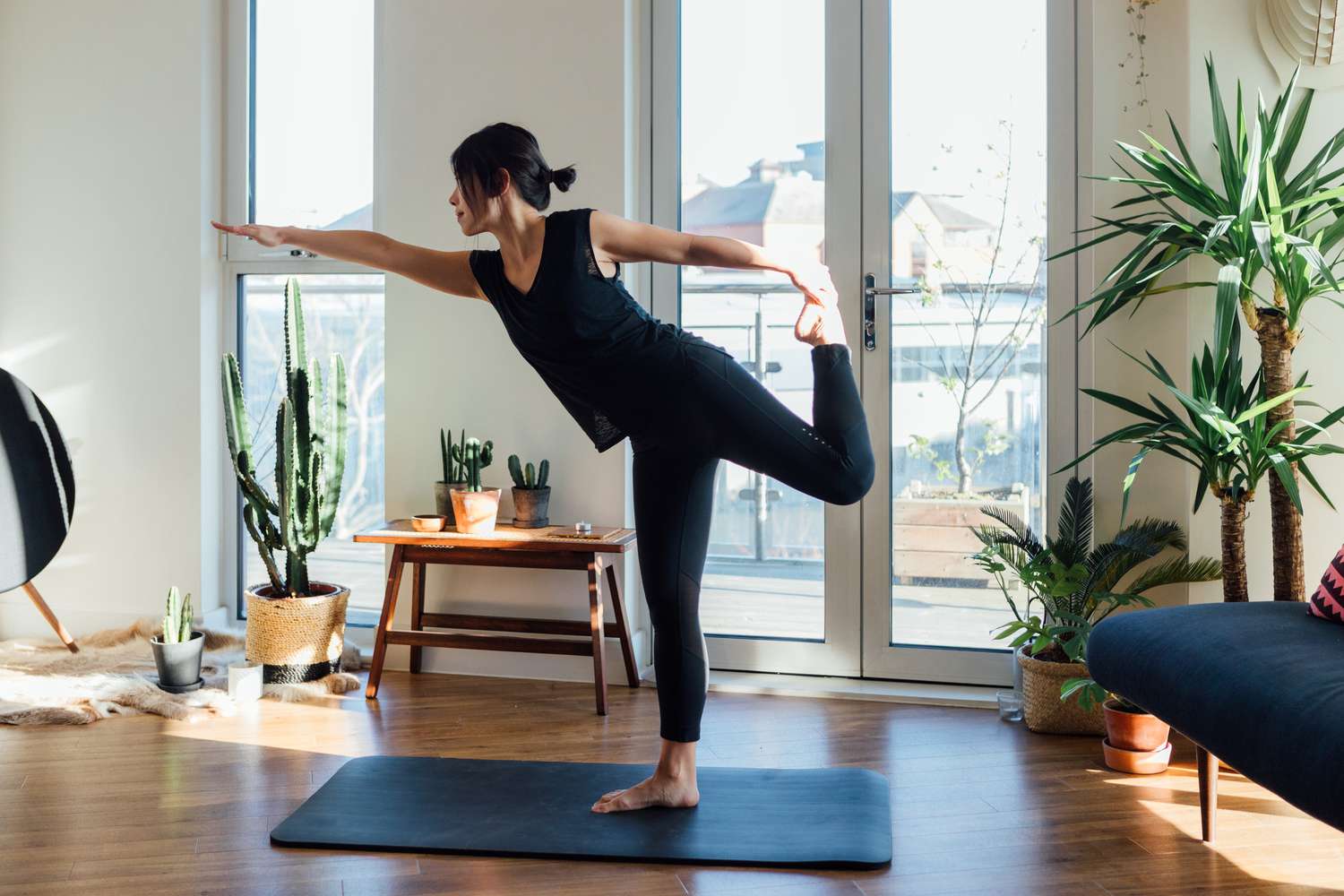 Woman performing single leg yoga pose in living room on yoga mat