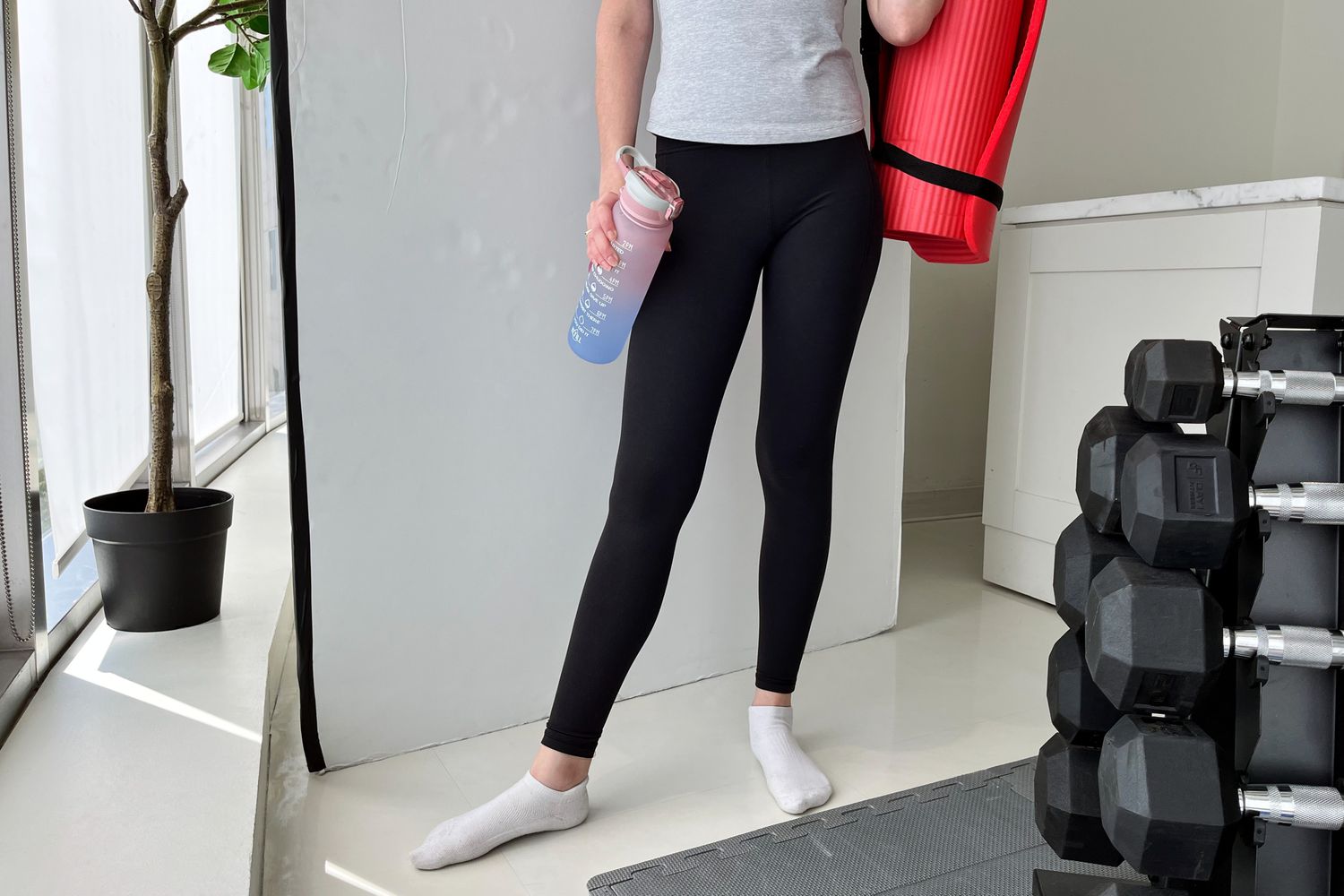 Person wearing Athleta leggings and holding a yoga mat and water bottle