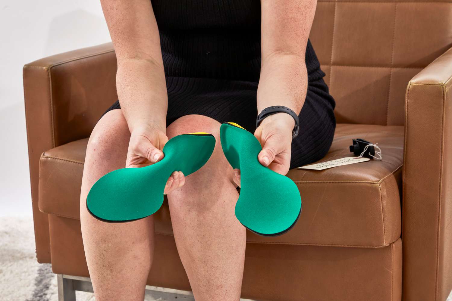 Person holding the Spenco PolySorb Cross Trainer Insoles while sitting on a brown leather armchair 