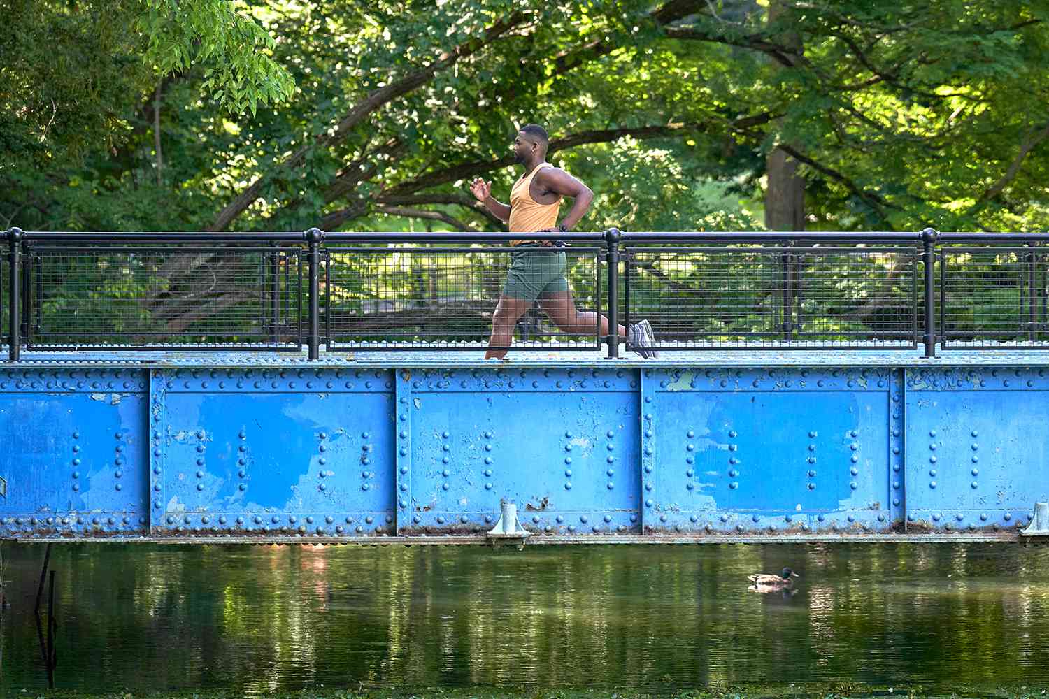 man running across a blue bridge with park in background