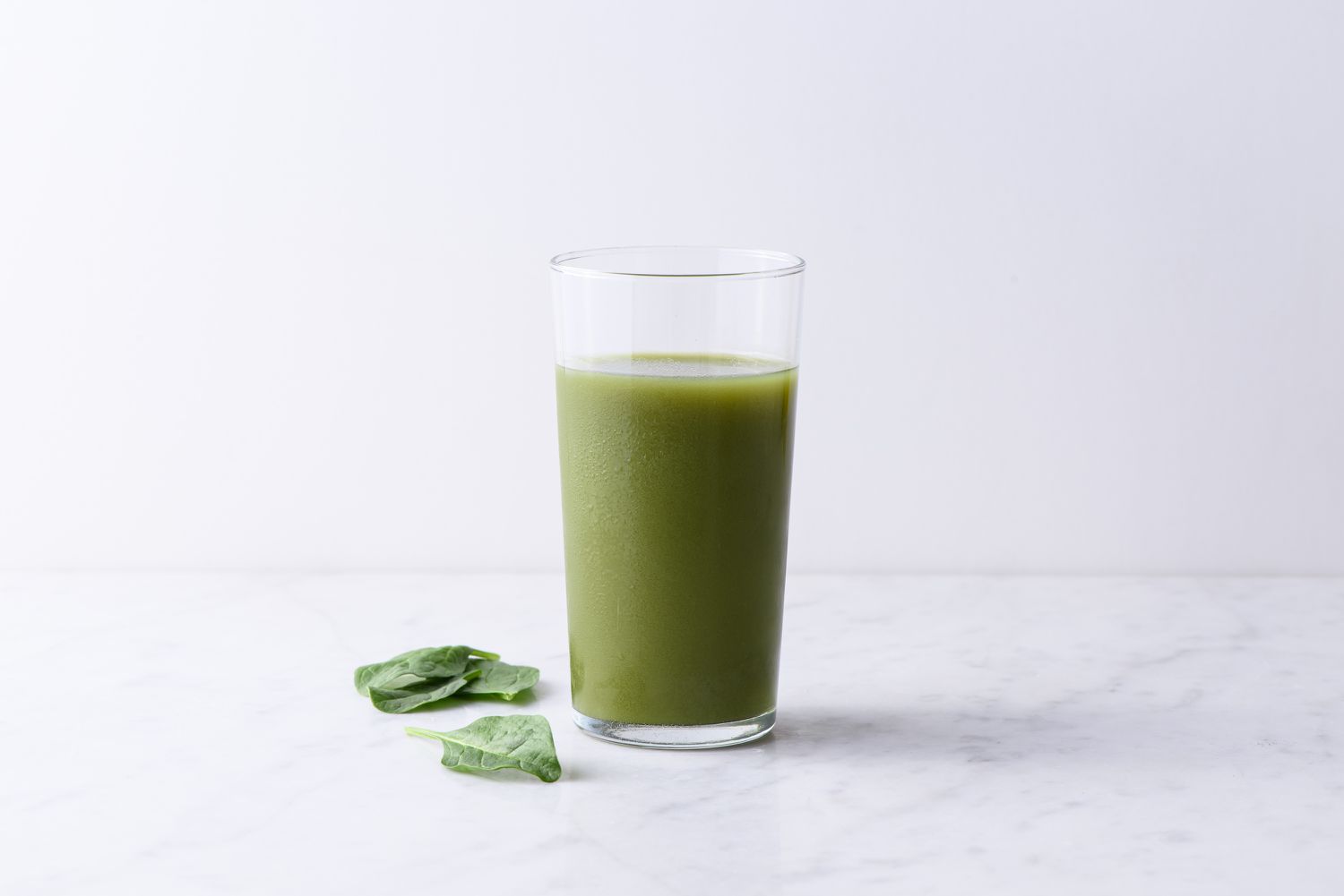 Glass of green juice displayed on a white surface