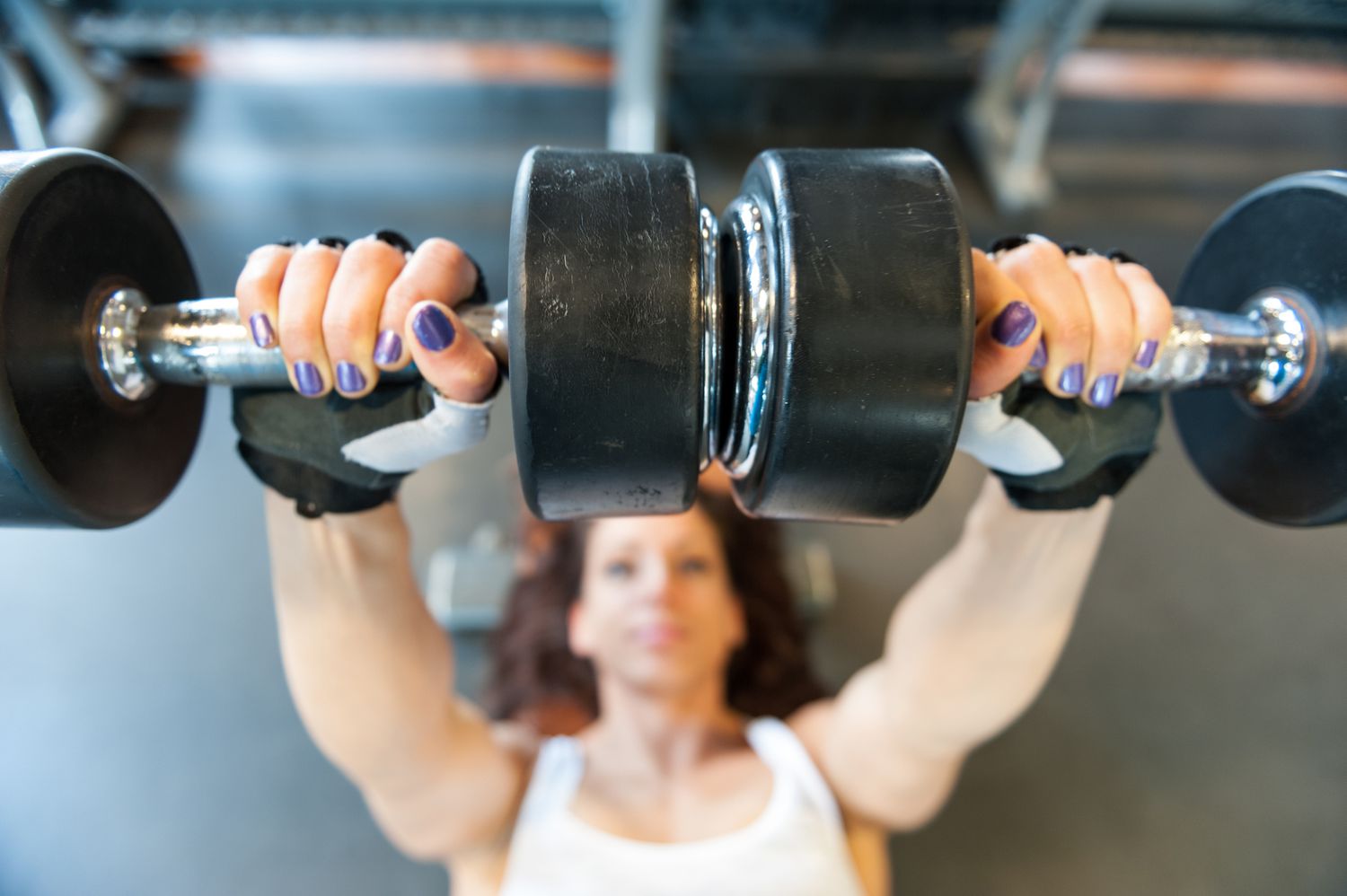 Young woman doing bench press with dumbbells at the gym.