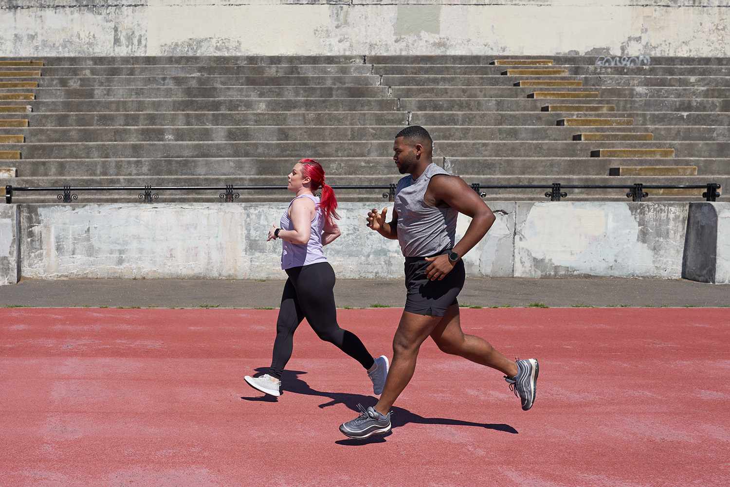 man and woman running on a track with steps in background