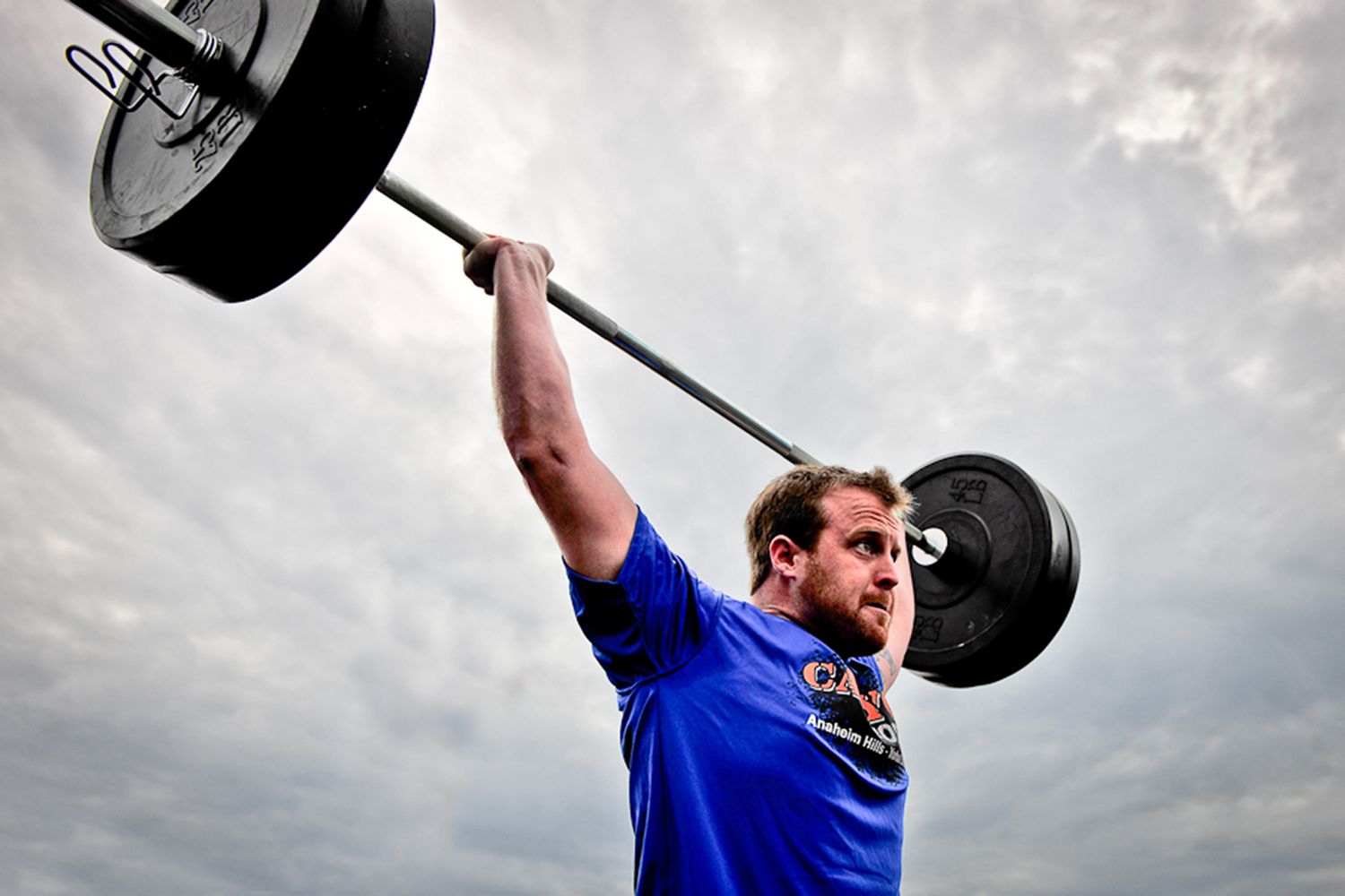 A man completes a push jerk overhead under grey skies.