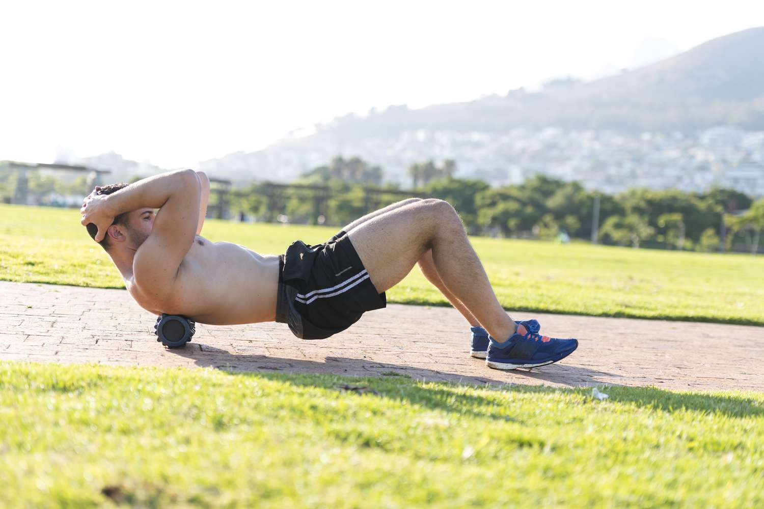 A young man performing exercises on a foam roller outdoors in a lush mountain area.