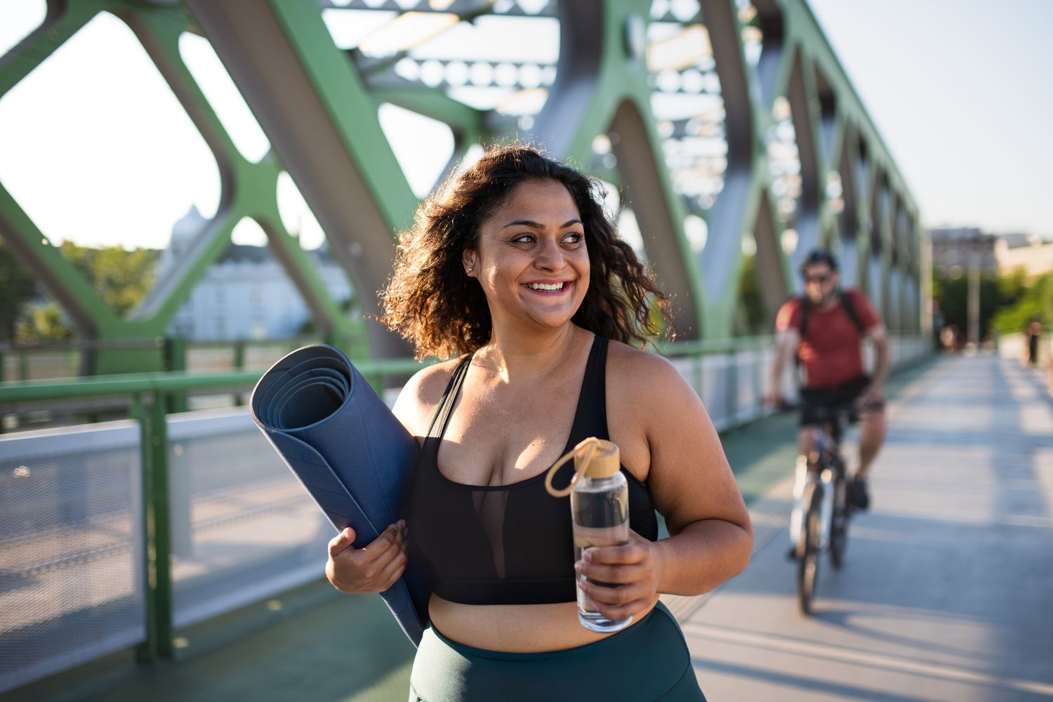 Woman walking on bridge with yoga mat and water bottle