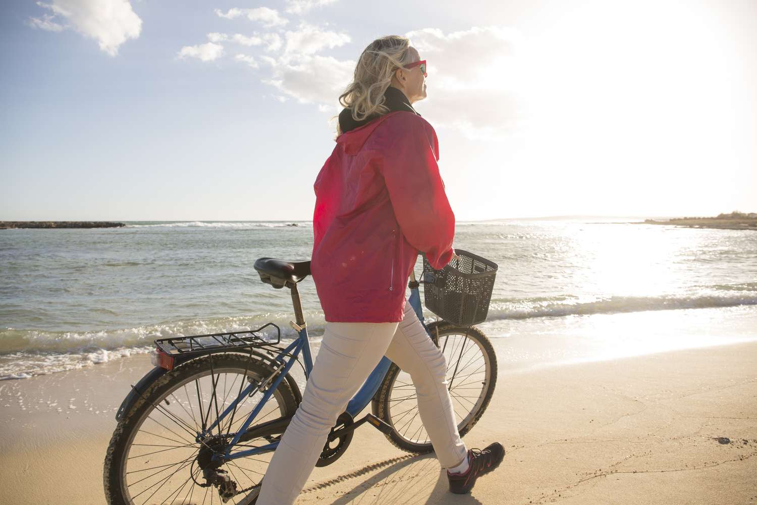 Woman pushes bike along sandy beach