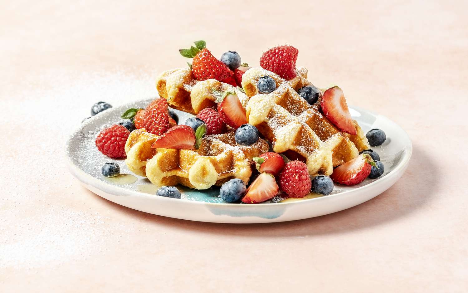 A plate of waffles with berries on peach background - stock photo