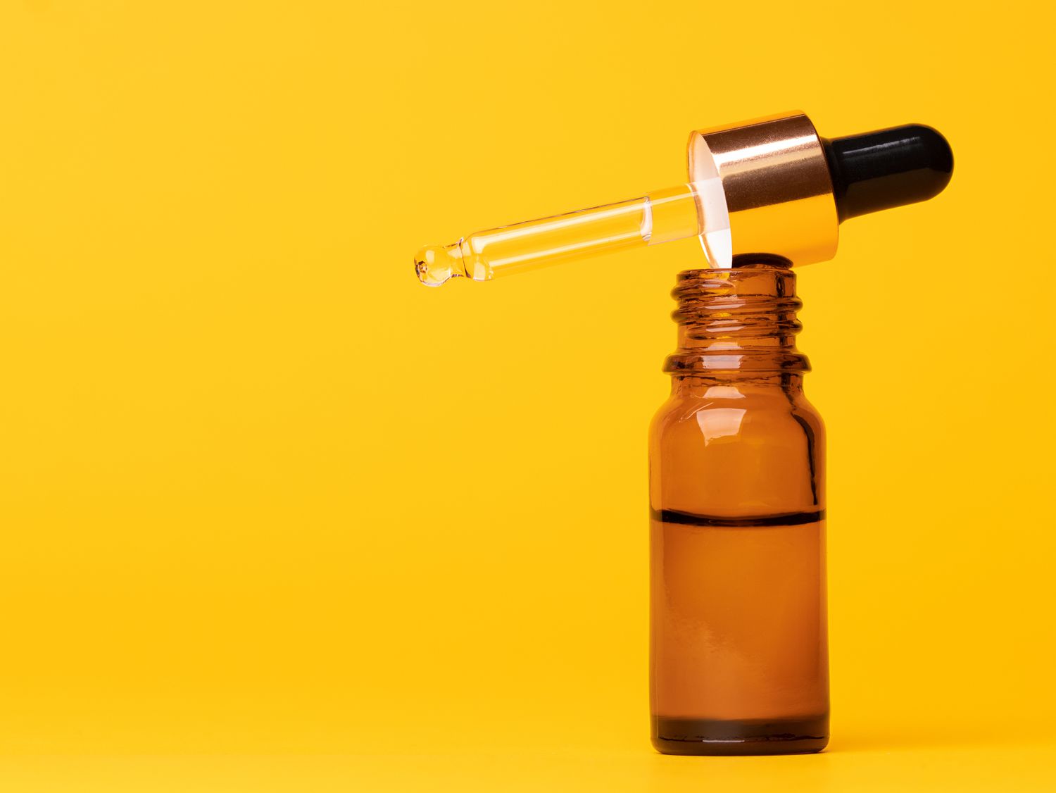 open tincture bottle, dropper filled with liquid, on yellow background