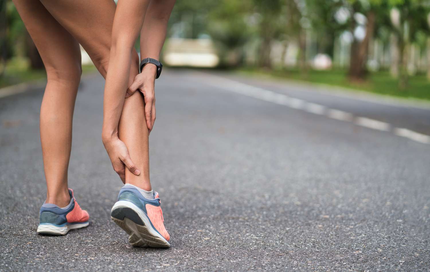 Achilles injury on running outdoors. Women holding Achilles tendon by hands close-up and suffering with pain. Ankle twist sprain accident in sport exercise running jogging.