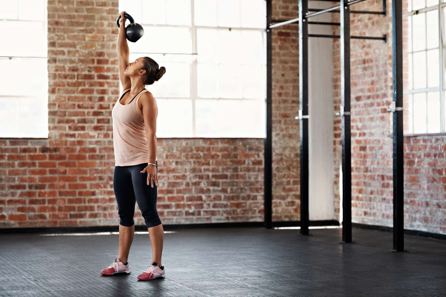 woman raising kettlebell over her head in an empty gym